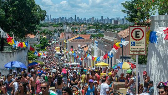 Oben angelangt, geniesst man die schöne Aussicht auf die Skyline von Recife, einer ältesten und grössten Städte von Brasilien. Auf der Strasse kommen tausende Menschen den Hügel hoch, man könnte denken, es findet eine religiöse Prozession statt. Religiös ist sie nicht, es ist Carneval …